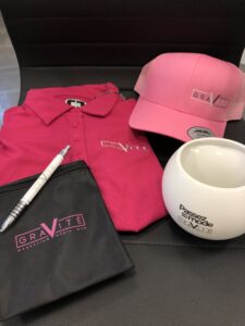 TERMINÉE – Enchère no 16 : un ensemble d&rsquo;items, dont un polo de golf fushia, à l&rsquo;effigie de Gravité Média